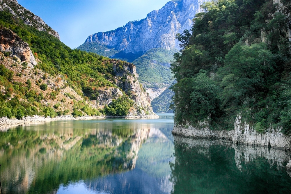 het Komanmeer in Albanië met aan de zijkanten rotsachtige kliffen die weerspiegelen in het water