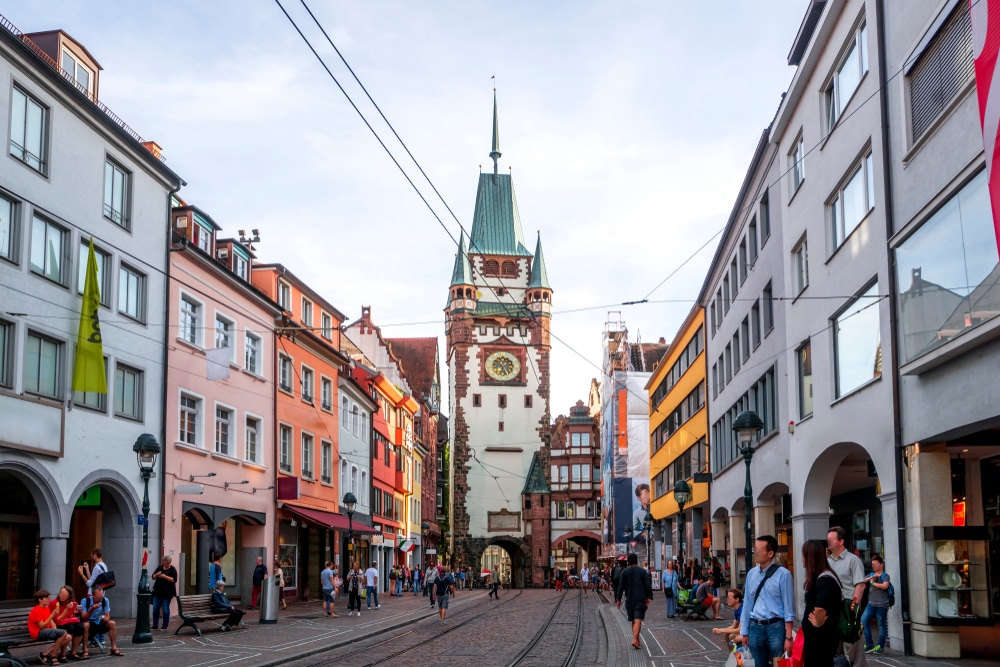 mensen die wandelen in een straat met gekleurde huizen en een trambaan in Freiburg im Breisgau