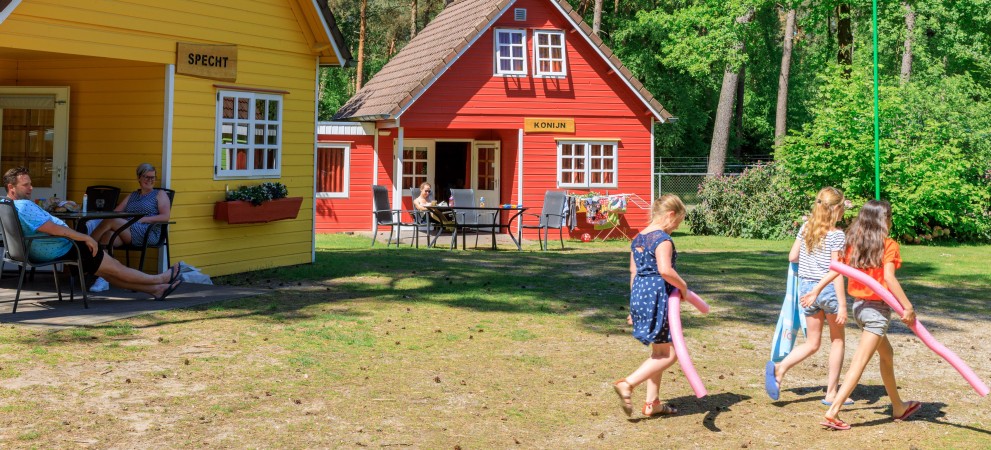 meisjes in zomerse outfits en met zwemspullen voor twee gekleurde huisjes op Ardoer Camping De Heldense Bossen