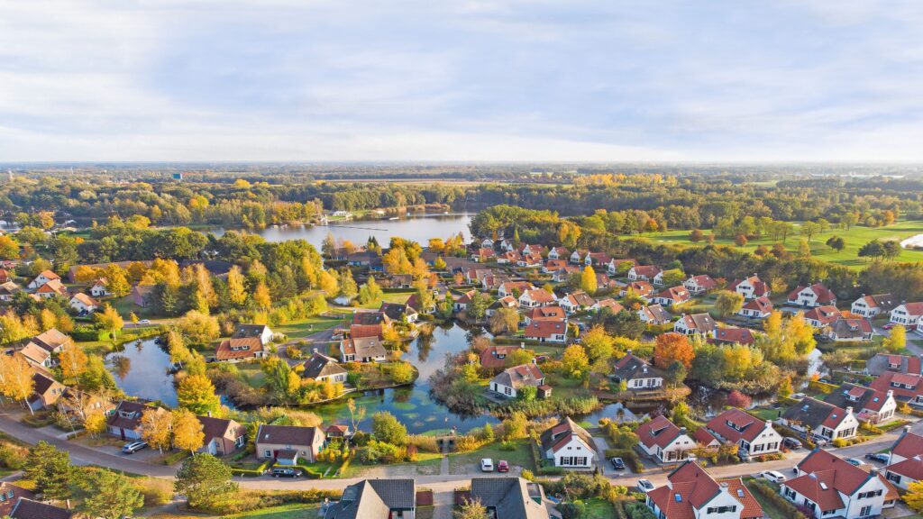 luchtfoto van Landal Vakantiepark Domein De Schatberg in de herfst. De bomen zijn geel en bruin gekleurd en de huisjes liggen aan het water.