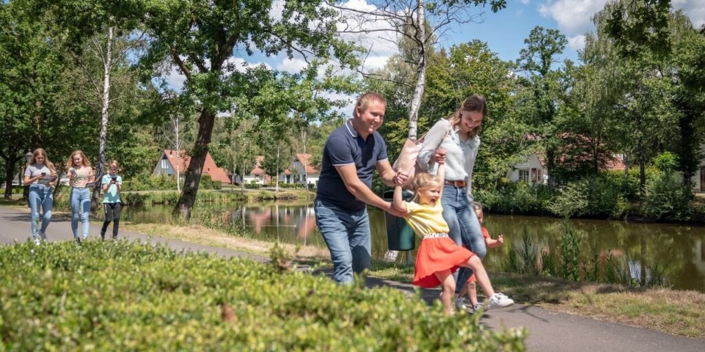 een vader en een moeder die met twee dochtertjes lopen. Achter het gezin lope ndrie kinderen met mobiele telefoontjes in hun handen op Landal Landgoed Aerwinkel.