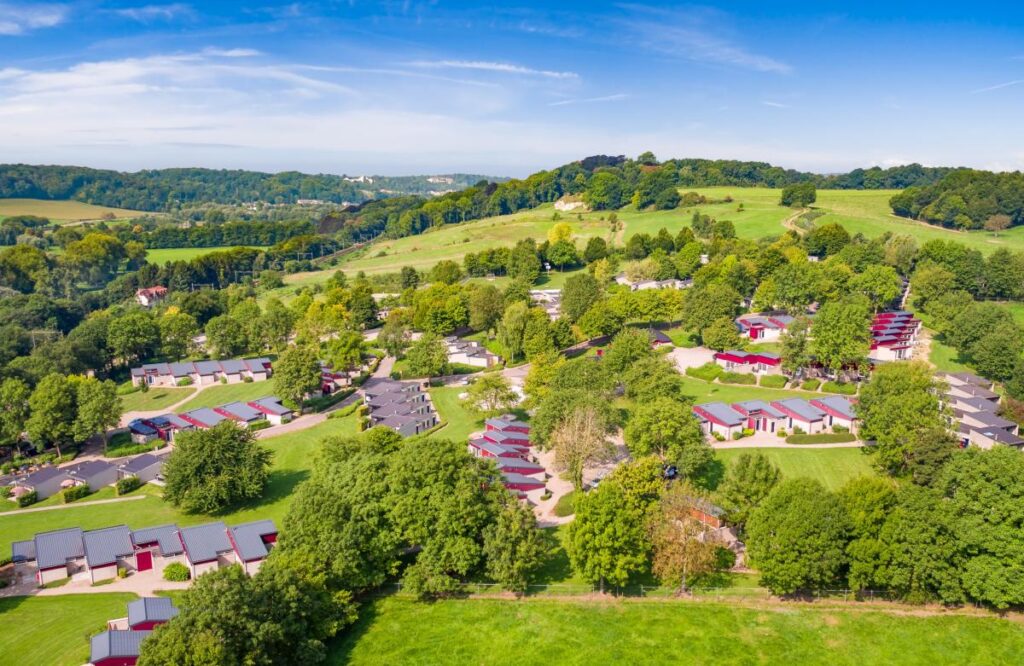 Bungalows gelegen op een groene heuvel met bomen op Roomport Bungalowpark Schin op Geul. De foto is van bovenaf genomen.