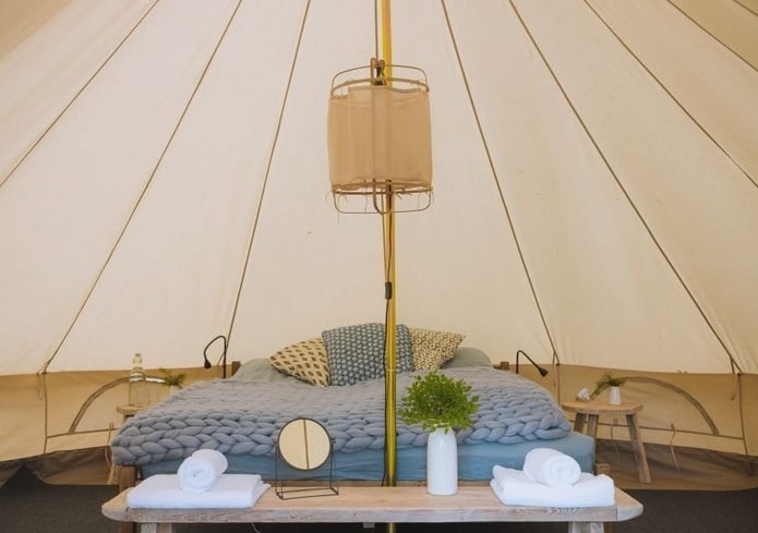 knus interieur van een Bell tent op Ameland met een opgemaakt bed en een lange, lage tafel met daarop handdoeken, een spiegeltje en vaas met bloemen