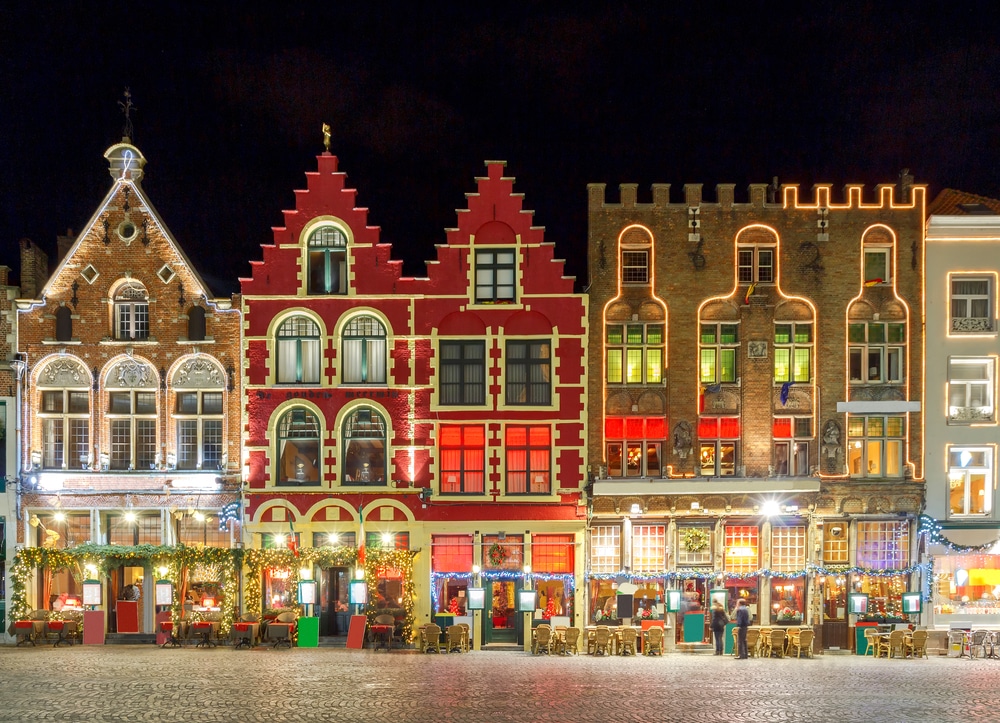 Plein met kleurrijke huizen die zijn versierd met kerstlichtjes in Brugge.