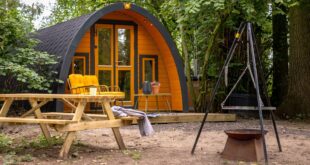 trekkersthut met een veranda met stoelen en tafeltje, een picknicktafel en een vuurschaal gelegen in een bos in Gelderland