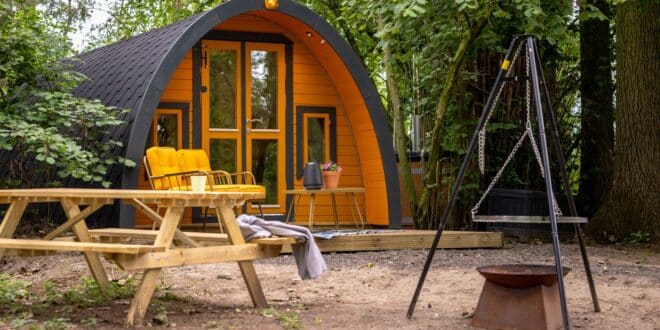 trekkersthut met een veranda met stoelen en tafeltje, een picknicktafel en een vuurschaal gelegen in een bos in Gelderland