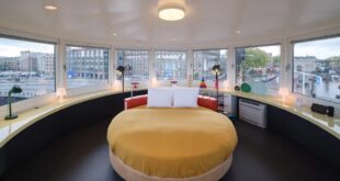 rond tweepersoonsbed in een ronde suite met panoramisch uitzicht op de straten en het water in Amsterdam