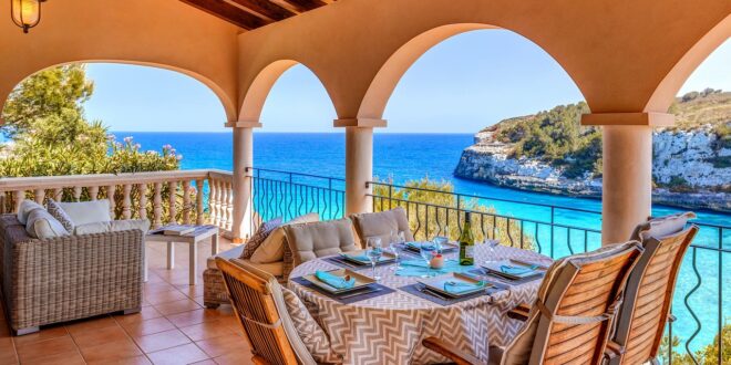 terras van een vakantiehuis met een gedekte tafel en een loungehoek en uitzicht op een azuurblauwe baai in Mallorca