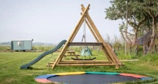 trampoline en een houten speeltoestel met glijbaan op een kleinschalig, groen kampeerterrein op het platteland van Texel
