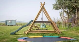 trampoline en een houten speeltoestel met glijbaan op een kleinschalig, groen kampeerterrein op het platteland van Texel