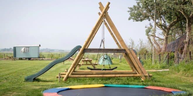 trampoline en een houten speeltoestel met glijbaan op een kleinschalig, groen kampeerterrein op het platteland van Texel