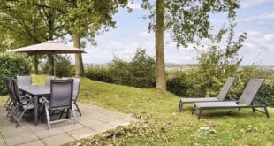 tuinstoelen aan een tuintafel met parasols en twee zonnebedjes bij een vakantiehuis op Landal Hoog Vaals. Vanaf het terras kijk je uit op een dal.