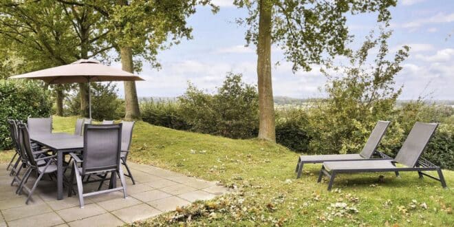 tuinstoelen aan een tuintafel met parasols en twee zonnebedjes bij een vakantiehuis op Landal Hoog Vaals. Vanaf het terras kijk je uit op een dal.