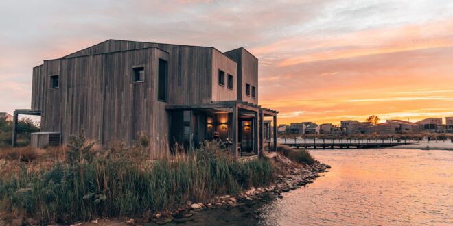 luxe houten bungalow met terras aan het water bij zonsondergang op vakantiepark Oasis Punt-West